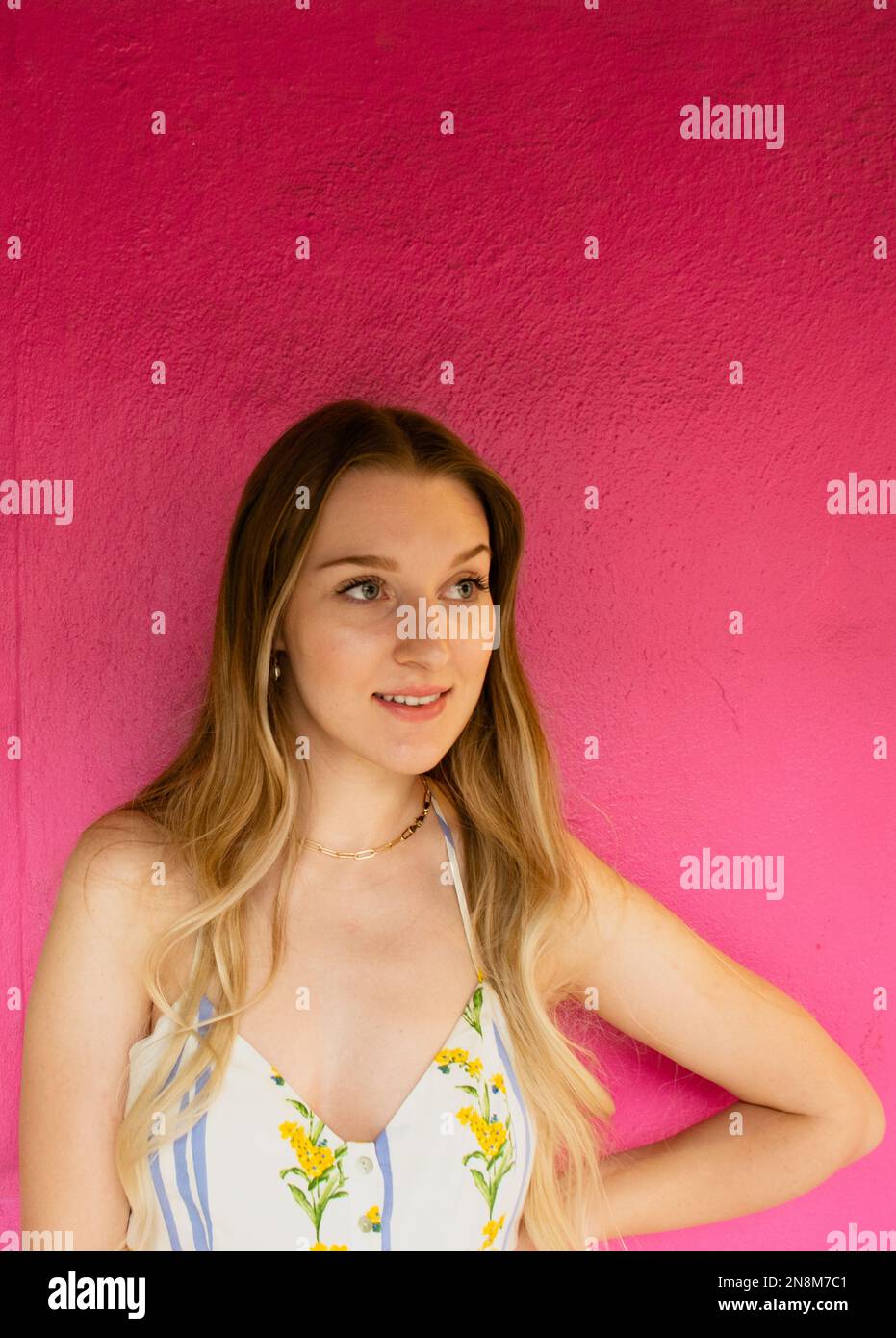 Ein blondes Mädchen, 20-35 Jahre alt, das an einer rosa Wand steht Stockfoto