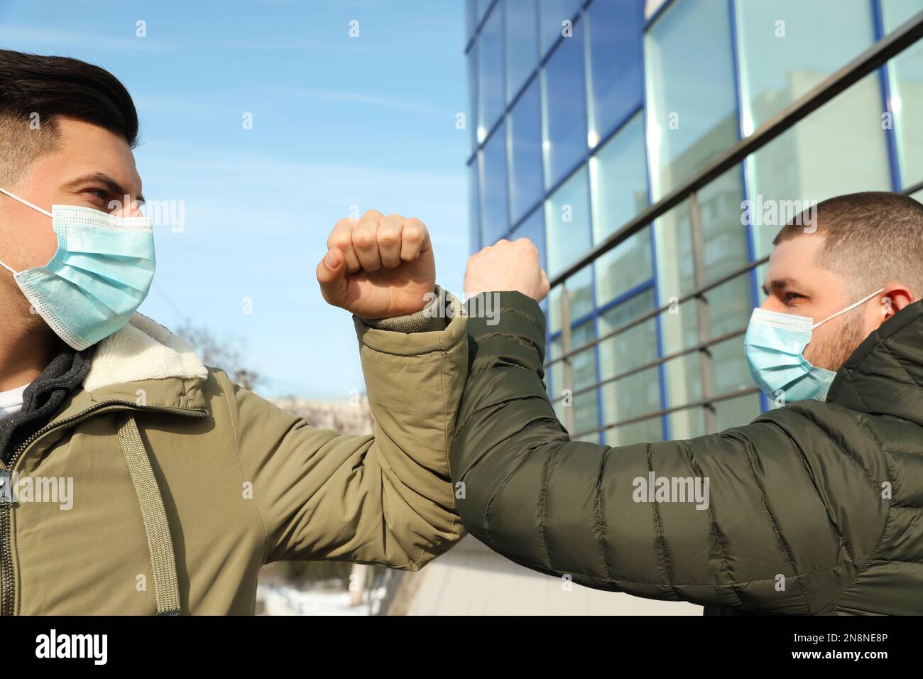 Männer in Masken begrüßen sich gegenseitig, indem sie im Freien Ellbogen stoßen Stockfoto