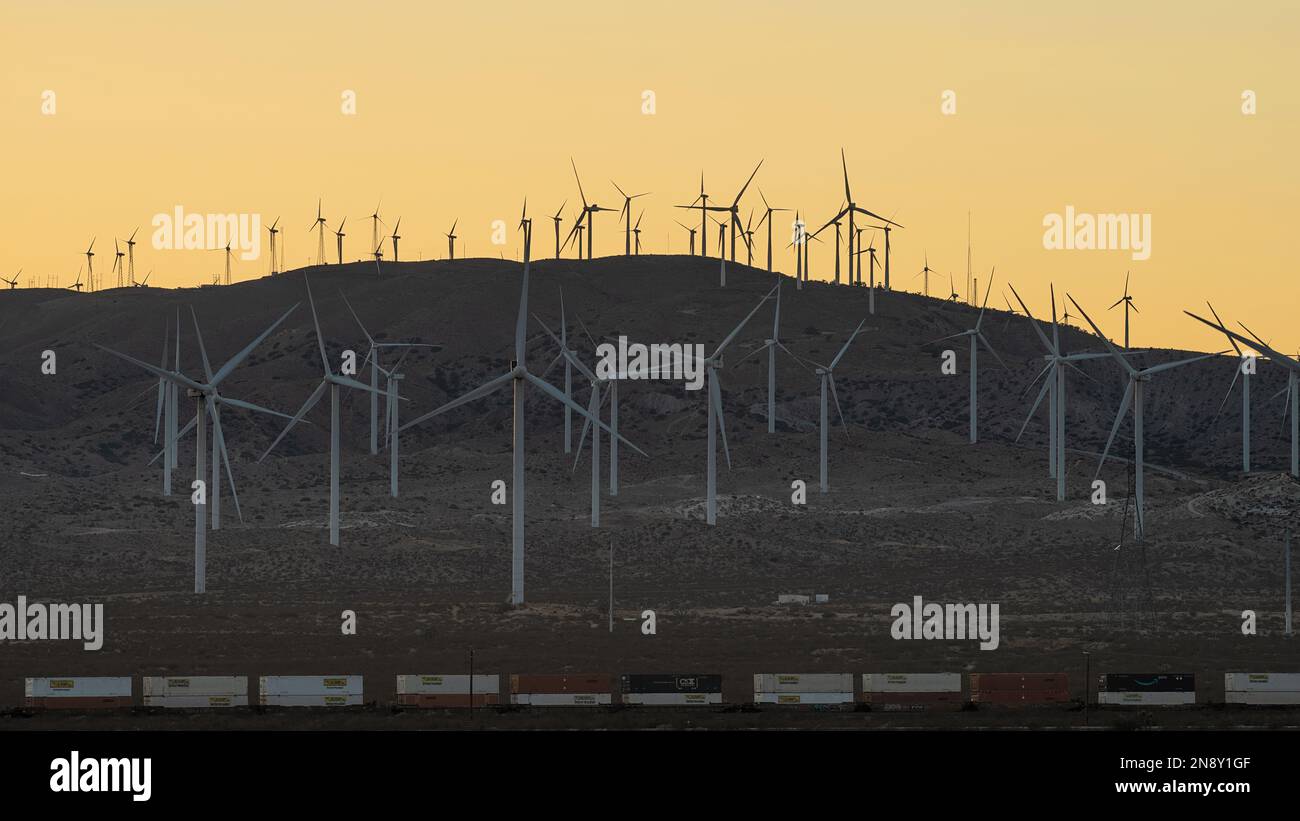 Windturbinen und ein vorbeifahrender Güterzug in der Abenddämmerung in der Nähe der Stadt Mojave in Kern County, Kalifornien, USA. Stockfoto