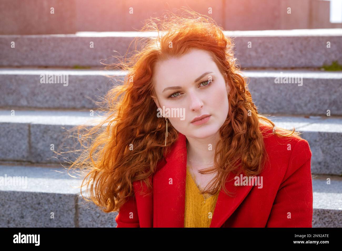 Nahaufnahme Porträt junge weiße Frau mit roten Locken im roten Mantel im Wind entwickelt Locken und genießt die Natur Stockfoto