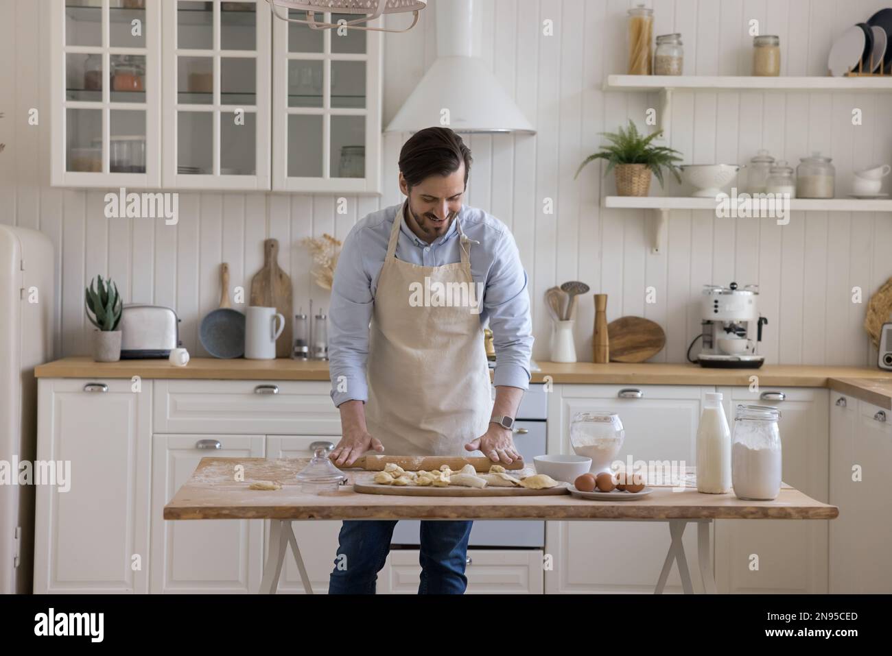 Positiver Bäckermann mit Schürze, rollender Teig auf dem Mehltisch Stockfoto