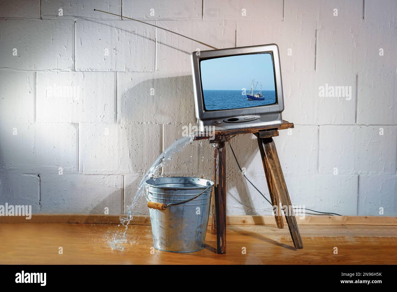 Ein alter Vintage-fernseher auf einem schrägen Holzhocker zeigt einen Film von einem Schiff auf dem Meer, aber das Wasser, das auf den Boden strömt, ohne den Eimer darunter. Gebh Stockfoto