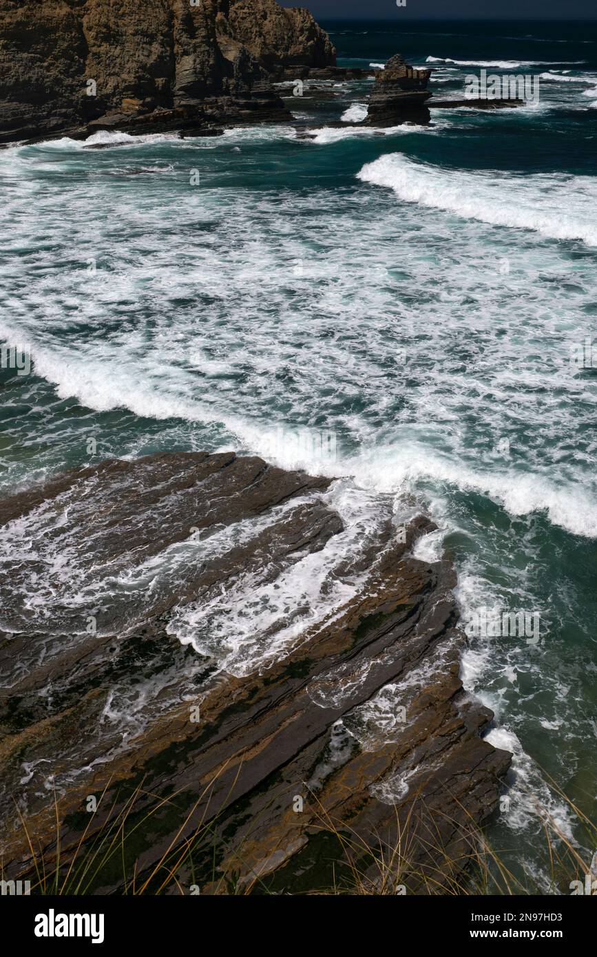 Weißer Schaum auf dunkelgrünem Wasser: Die rauschenden Atlantikwellen schwirren um Felsen und schlängeln sich über geschichtete Platten entlang der zerklüfteten Küste von Cabo Carvoeiro in Peniche im Stadtteil Leiria im Zentrum Portugals. Mit den Berlenga-Inseln etwa 10 km vor der Küste ist das Cape ein Naturschutzgebiet mit einer vielfältigen Meeres- und Vogelwelt - aber immer eine extreme Gefahr für die Schifffahrt. Stockfoto