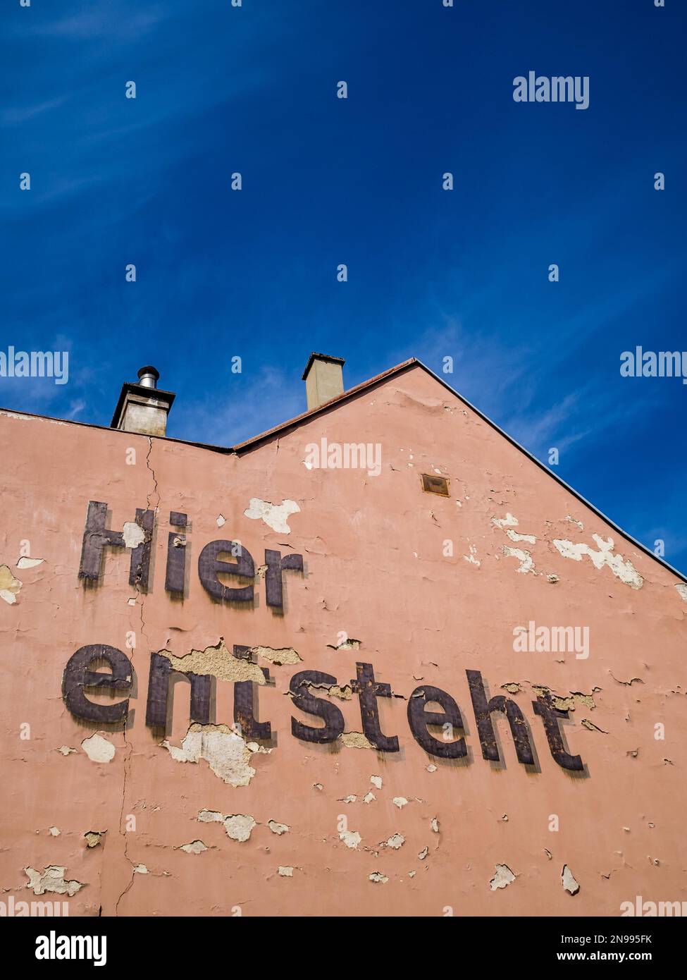 Hier erhebt sich die Ankündigung eines Bauprojekts an einer lachsfarbenen Hauswand Stockfoto