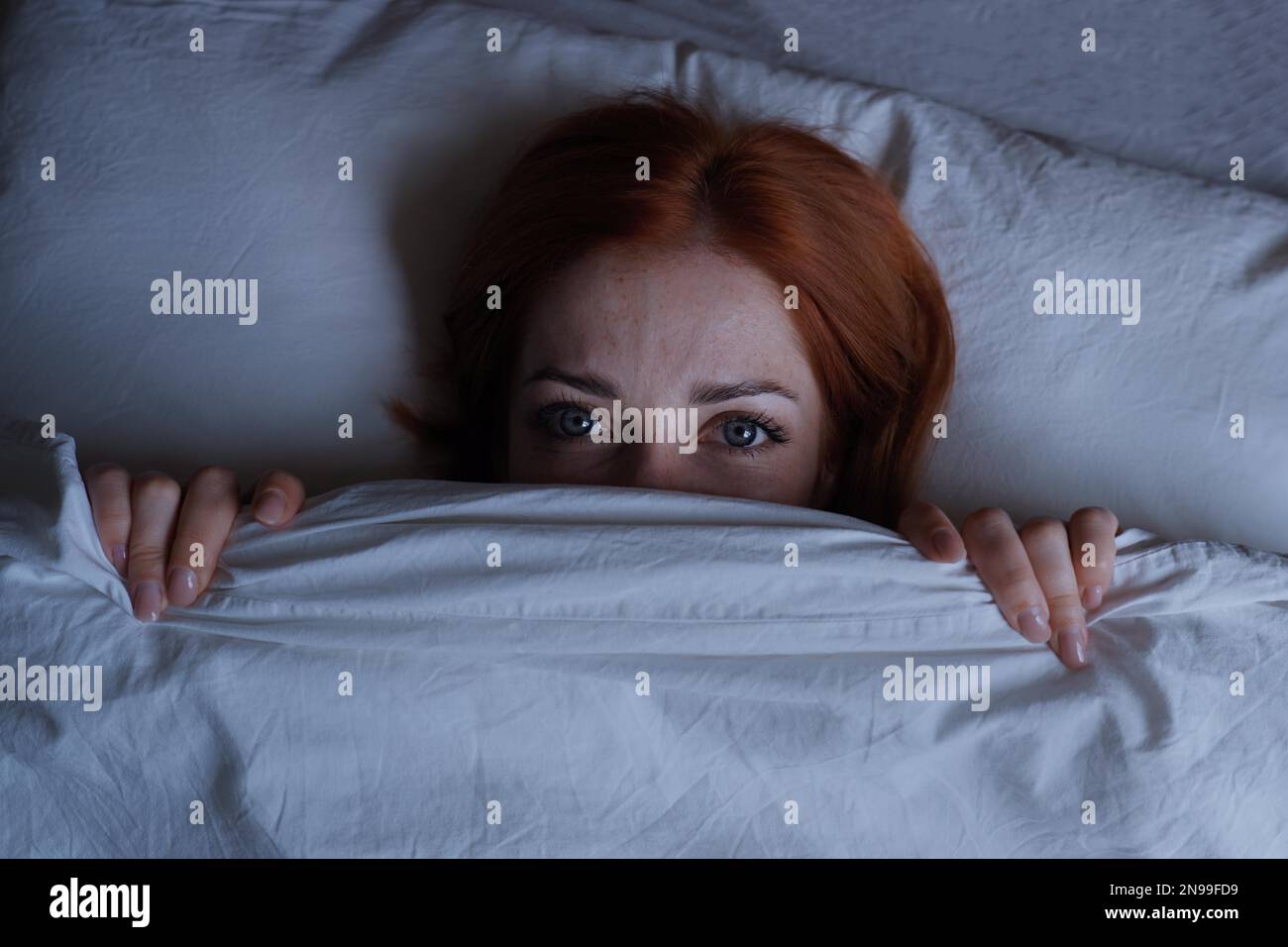 Schlaflose Frau liegt im Bett mit offenen Augen, die sich nachts unter der Bettdecke verstecken Stockfoto