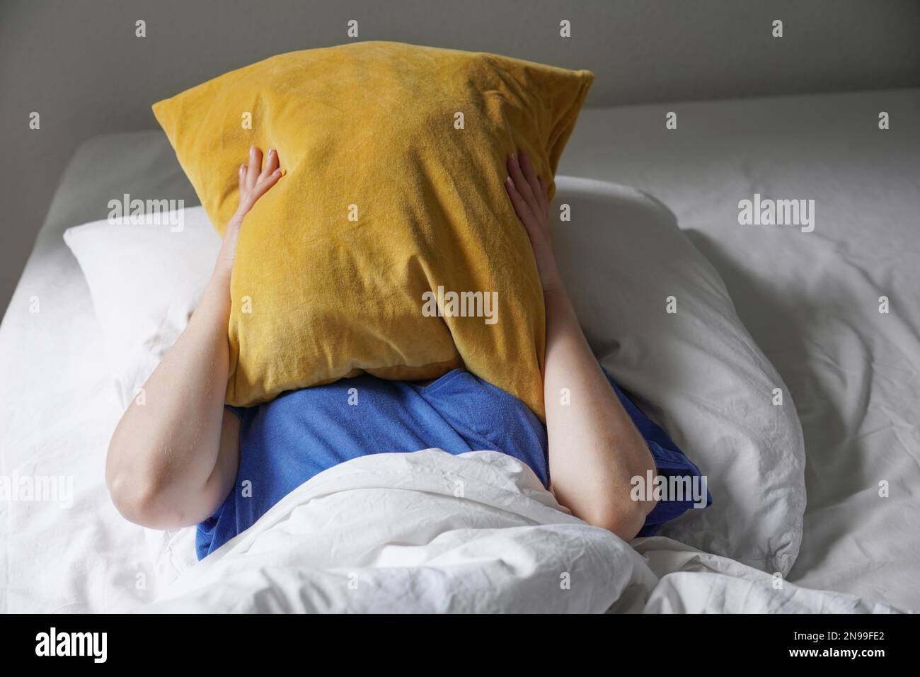 Nicht erkennbare Person, die im Bett liegt und sich unter dem Kissen versteckt, fühlt sich müde und lustlos Stockfoto