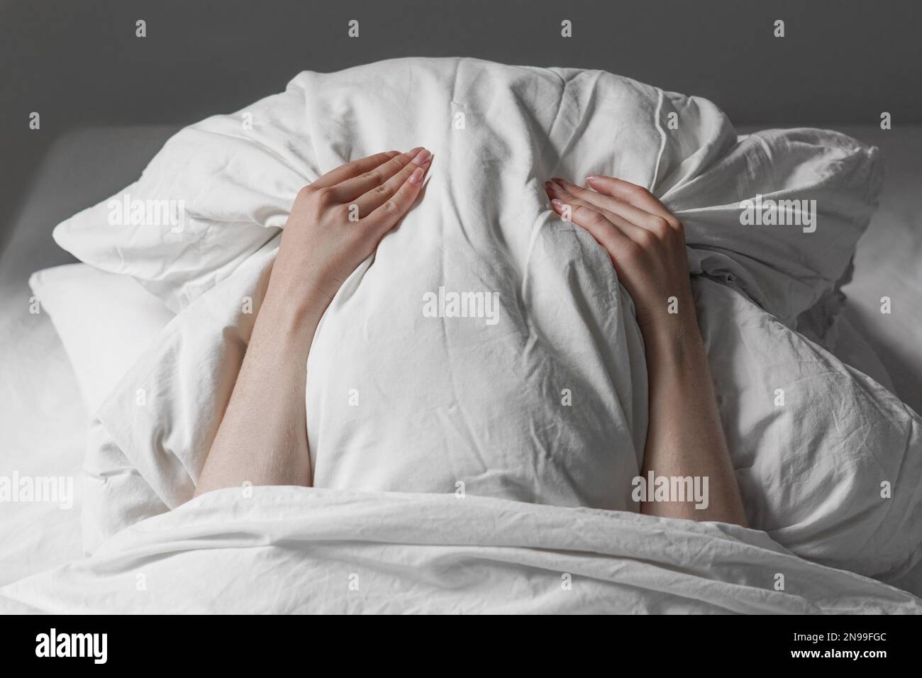 Eine nicht wiedererkennbare Frau im Bett bedeckte das Gesicht unter dem Kissen, um sich früh am Morgen vor Sonnenlicht zu verstecken Stockfoto