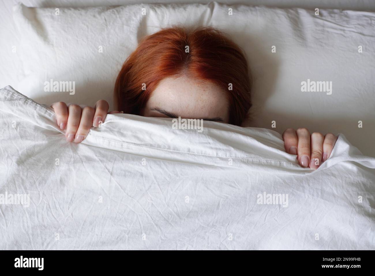 Eine Frau versteckt ihr Gesicht vor Sonnenlicht unter der Decke und weigert sich aufzustehen Stockfoto