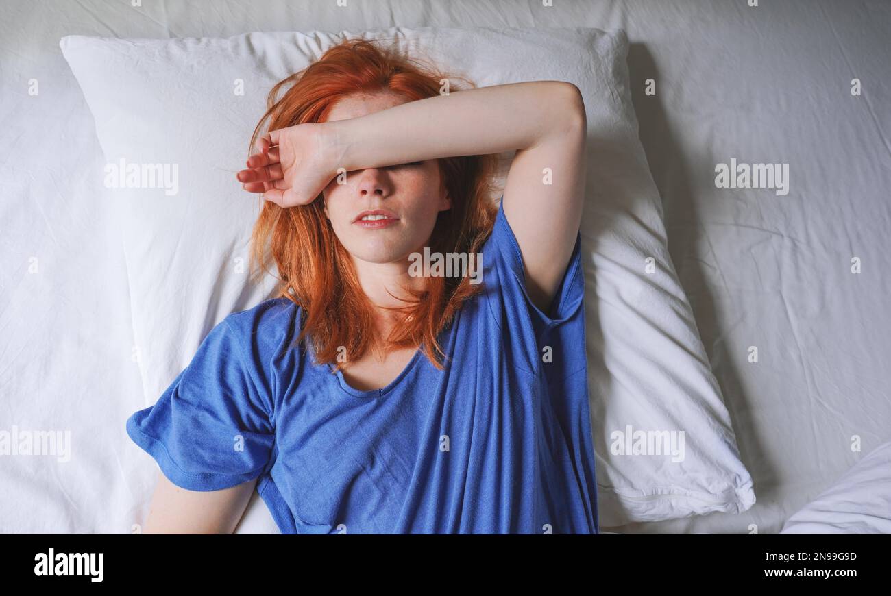 Junge Frau liegt im Bett mit Migräne und Lichtempfindlichkeit, die ihre Augen bedeckt Stockfoto