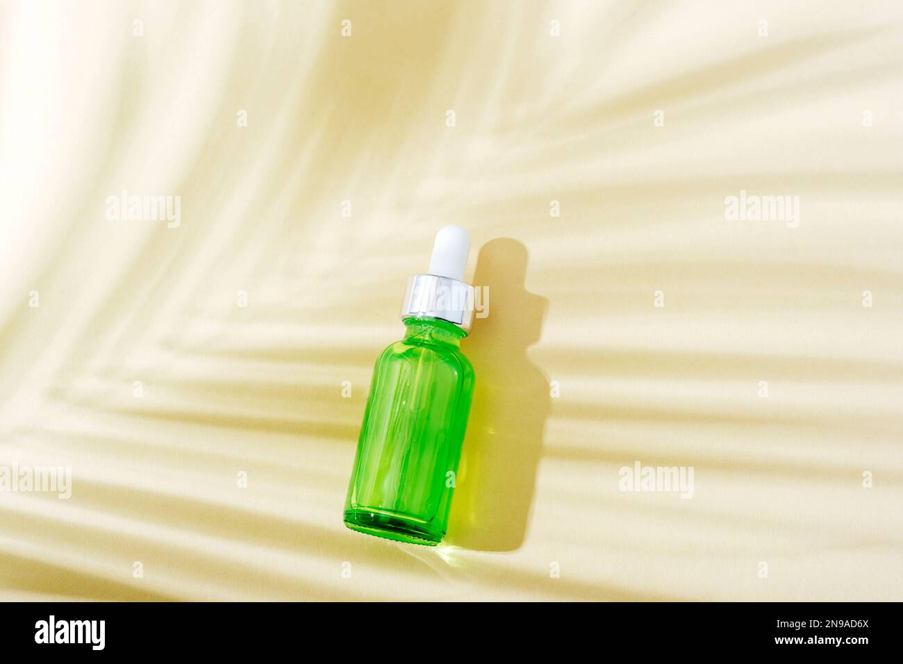 Grüne Kosmetikflasche zur Gesichtspflege und Palmenblattschatten. Draufsicht, flach liegend. Stockfoto