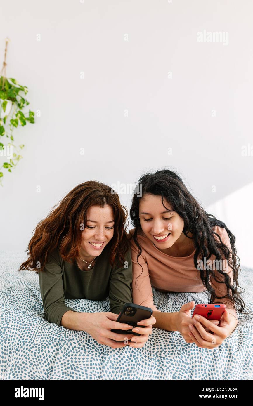 Vertikale Aufnahme von zwei Mädchen im Teenageralter, die ihr Smartphone zusammen im Bett benutzen Stockfoto