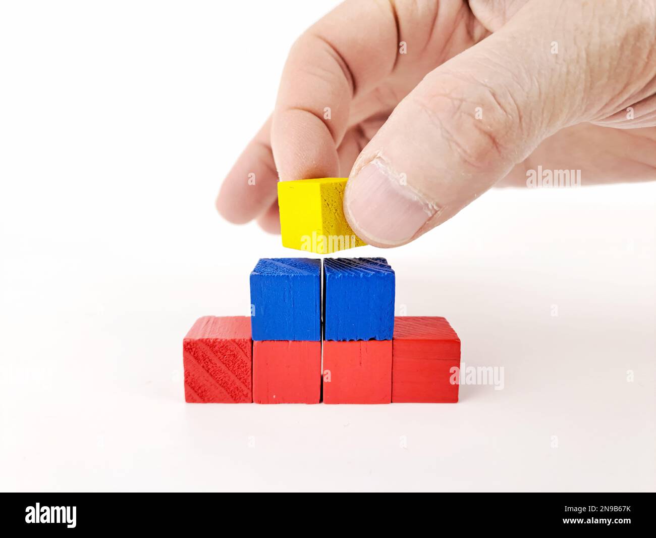 Abstrakte, mehrfarbige 3D-Pyramiden-Karte auf weißem Hintergrund, mit der Hand eines reifen Mannes. Stockfoto Abstrakte, mehrfarbige 3D-Pyramiden-Karte auf weißem Hintergrund, mit der Hand eines reifen Mannes. Stockfoto