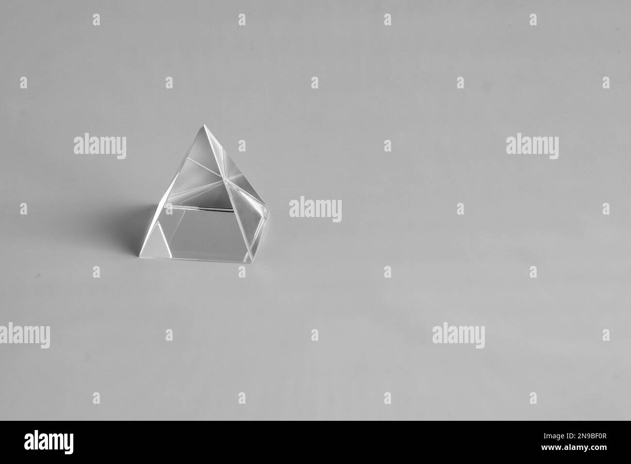 Kristallpyramide auf grauem Hintergrund. Scharfe Kanten. Gespiegelte Flächen. Zahlreiche Reflexionen und Lichtbrechung. Abstraktes geometrisches Muster. Selektiv Stockfoto