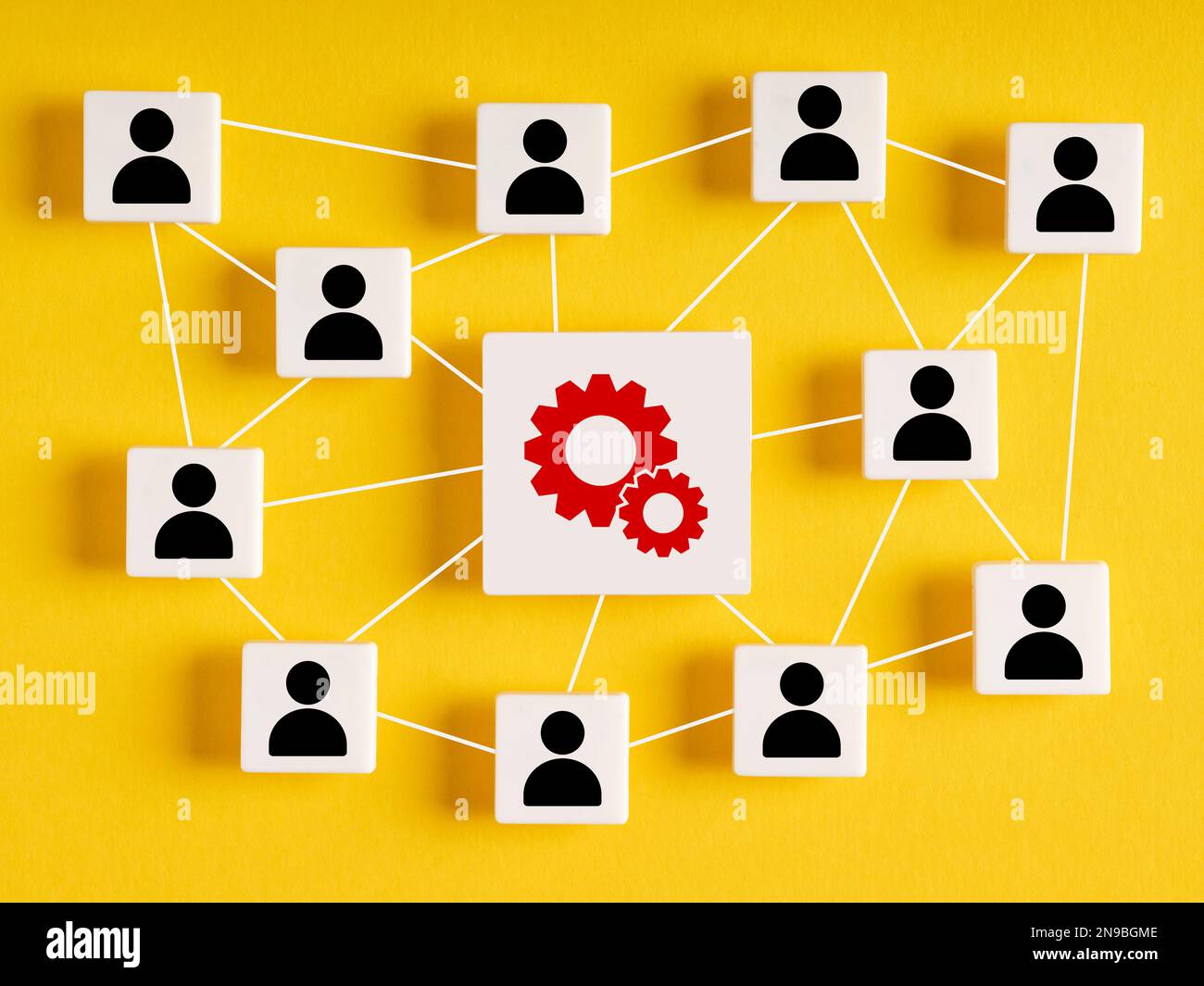 Unternehmensproduktionsnetzwerk. Verbindung zwischen Produktivität und Teamarbeit. Würfel mit Menschen- und Zahnradsymbolen auf gelbem Hintergrund. Stockfoto