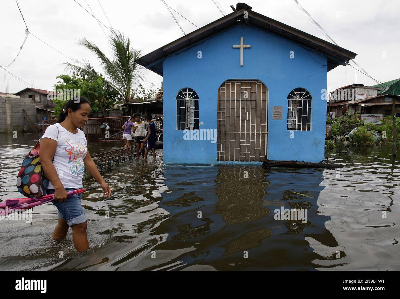 A Filipino woman passes by a flooded chapel at Valenzuela city, north of Manila, Philippines on Tuesday July 31, 2012. Typhoon Saola dumped torrents of rain as it swept past the Philippines, killing at least seven people and displacing more than 20,000 others by Tuesday. (AP Photo/Aaron Favila) Stockfoto