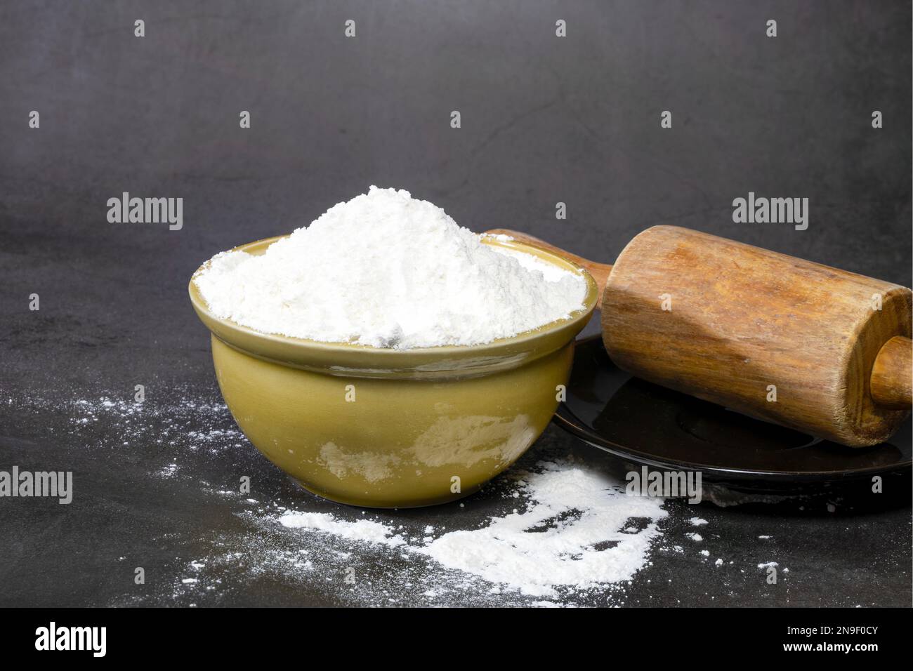 Eine braune Keramikschüssel mit Allzweckmehlpulver auf schwarzem Hintergrund. Stockfoto