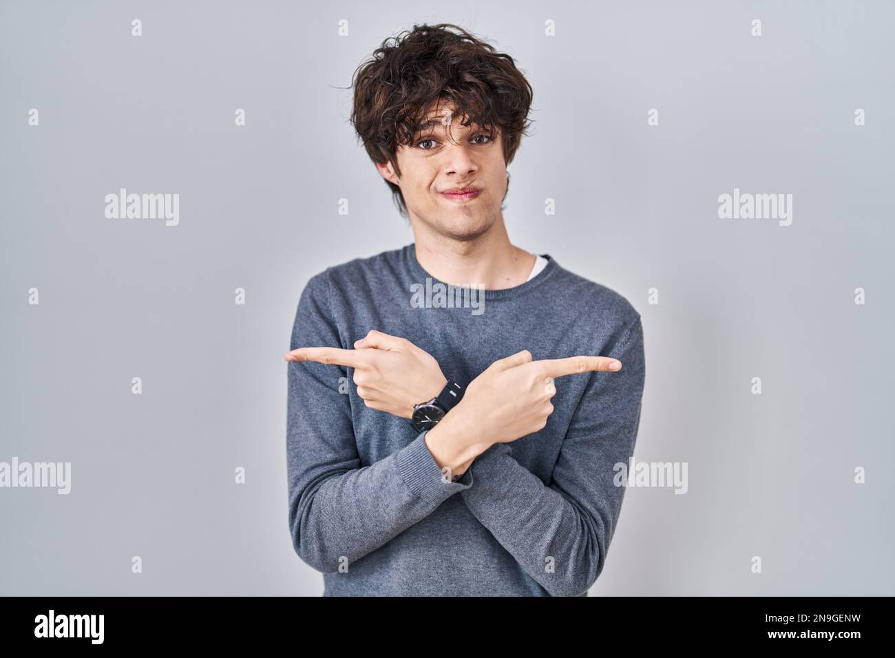 Der junge Mann, der über einem isolierten Hintergrund mit Fingern auf beide Seiten zeigt, ist in eine andere Richtung nicht einverstanden Stockfoto
