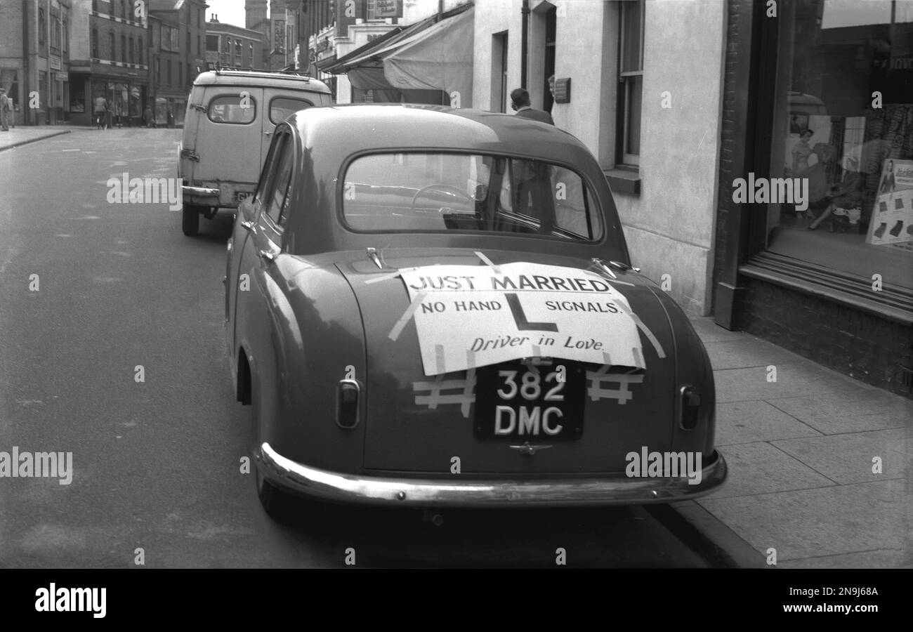 1950er Jahre, historisch, ein Auto der Epoche, geparkt in einer Hauptstraße, Linclon, England, Großbritannien, mit einer großen L-Platte auf dem Kofferraum des Autos. Das Zeichen lautet... "Gerade Verheiratet"... „Keine Handsignale“, „Fahrer in Liebe“. Stockfoto