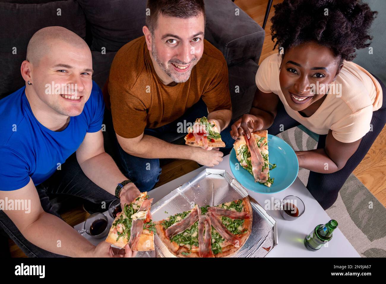 Eine Gruppe junger Freunde, die Pizza essen. Heimmannschaft. Großer Blickwinkel. Ich schaue in die Kamera. Stockfoto