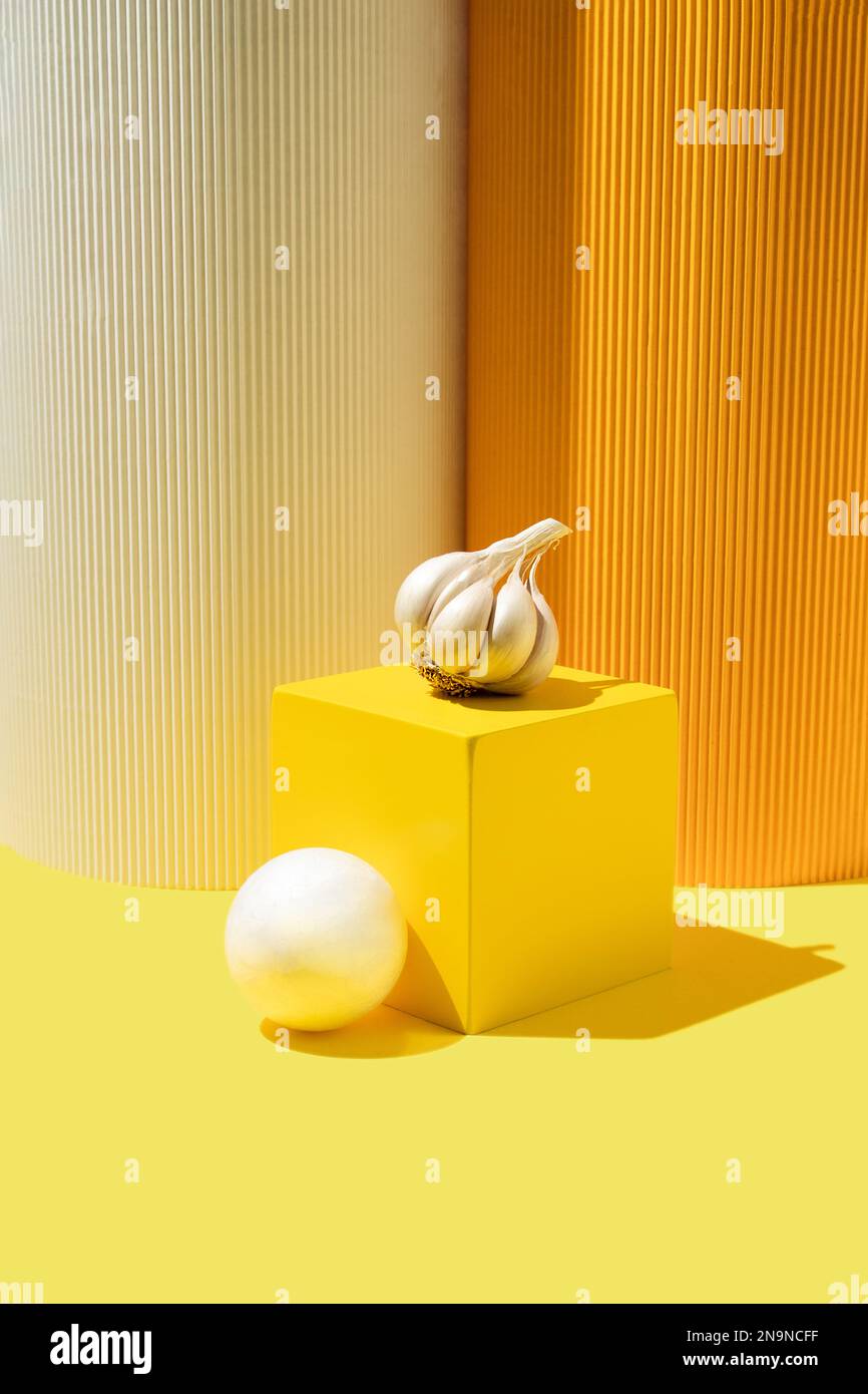 Frischer Knoblauch auf einem gelben würfelförmigen Ständer. Minimales geometrisches Konzept. Stockfoto