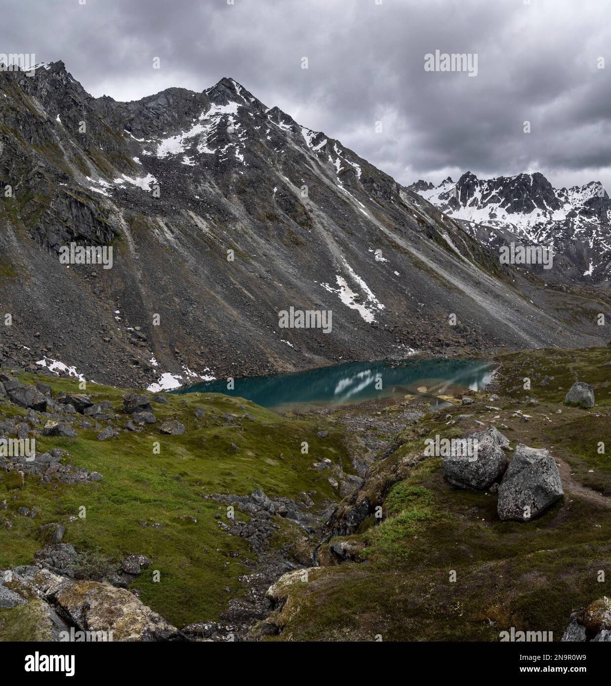 Granitgipfel am Hatcher Pass unter einem grauen, wolkigen Himmel mit dem dunklen türkisfarbenen Wasser der Reed Lakes in der Nähe der Independence Mine Stockfoto