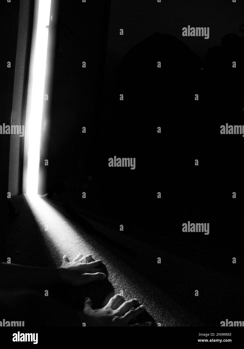 Eine vertikale Grauskala von Händen auf dem Boden unter dem Licht, das von der Tür kommt Stockfoto