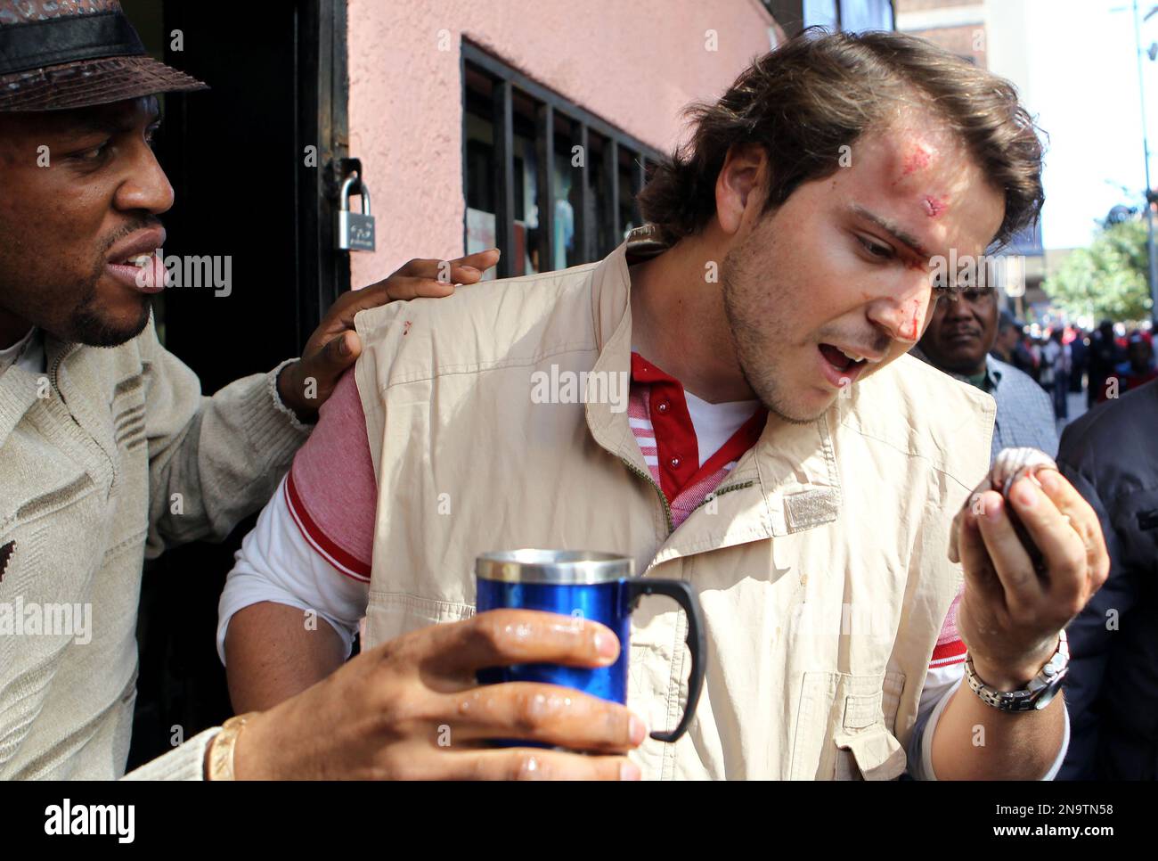 South Africa's M&G journalist Nickolaus Bauer is assisted by a shop owner after being hit by a stone during a protest by opposition party Democratic Alliance (DA) supporters against the Congress of South African Trade Unions (Cosatu) for opposing the youth wage subsidy in Johannesburg, South Africa on Tuesday May 15, 2012. An opposition party march in Johannesburg turned violent Tuesday after union supporters hurled rocks at the leader of South Africa's main opposition party. (AP Photo/Themba Hadebe) Stockfoto