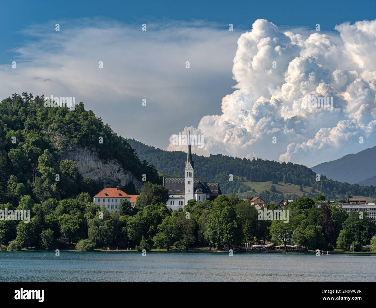 Bleder See mit einer Kirche Zupnijska cerkev svetega Martina - Kirche St. Martina, Bled, mit einem Hintergrund von weißen Wolken am Sommertag Stockfoto