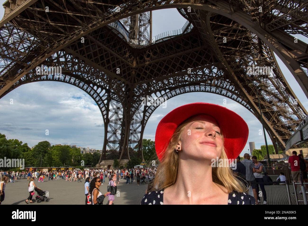Junge Frau mit rotem Hut steht unter dem Eiffelturm und sonnt sich im Sonnenlicht in Paris, Frankreich, Paris, Frankreich Stockfoto