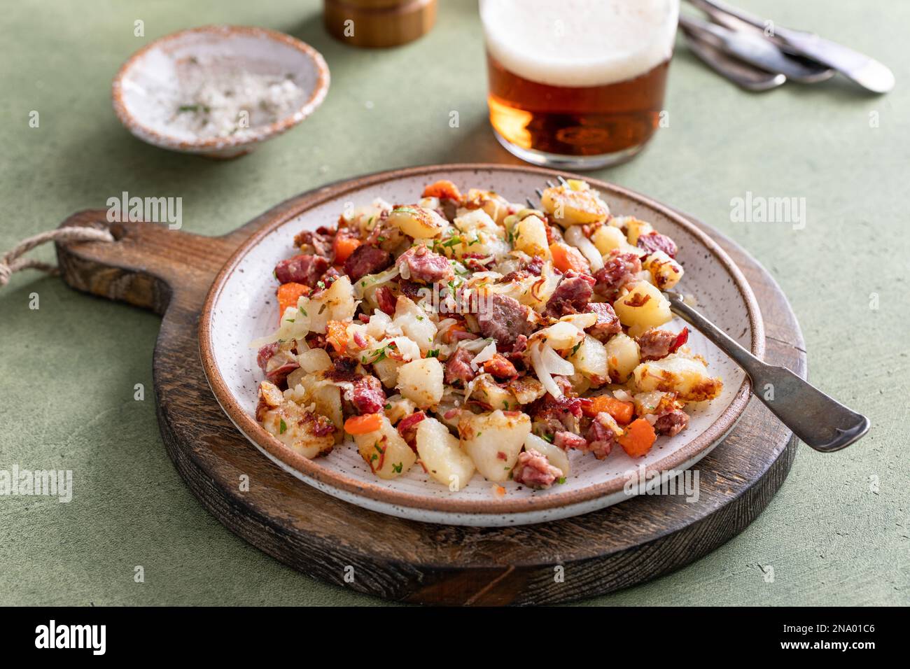 Corned Beef Hash mit Kartoffeln, Kohl und Karotten auf einem Teller serviert mit Bier Stockfoto