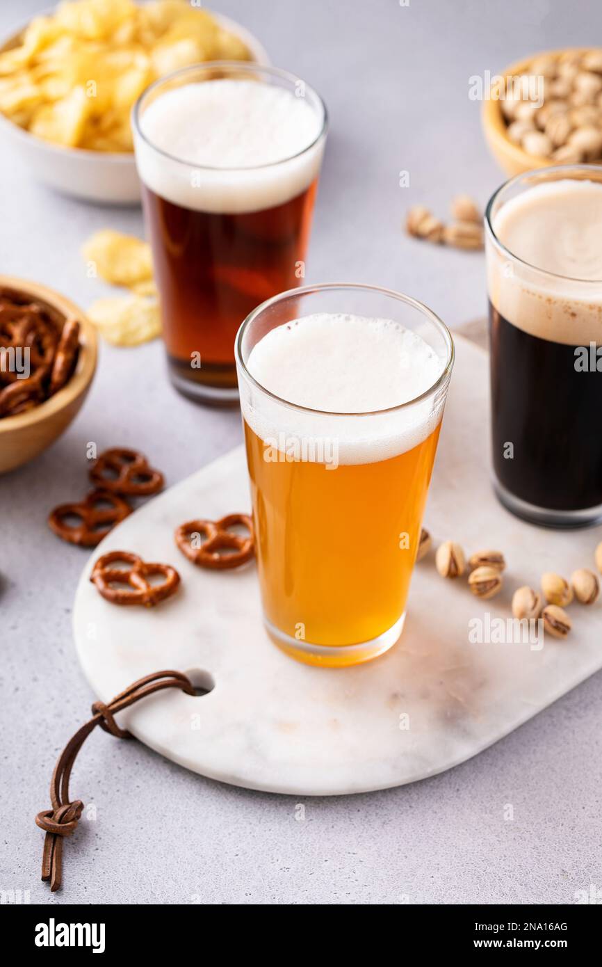 Verschiedene Biersorten mit dunklem Stout, traditionellem Lager und belgischem Weiß, serviert mit Snacks auf dem Tisch Stockfoto