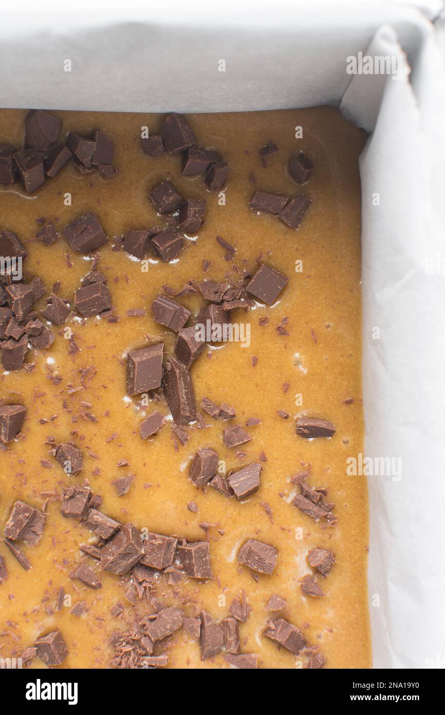 Blondie-Teig mit Schokoladenstückchen in einer mit Pergament ausgekleideten quadratischen Backform, Kuchenteig in einer 10 cm großen Backform Stockfoto