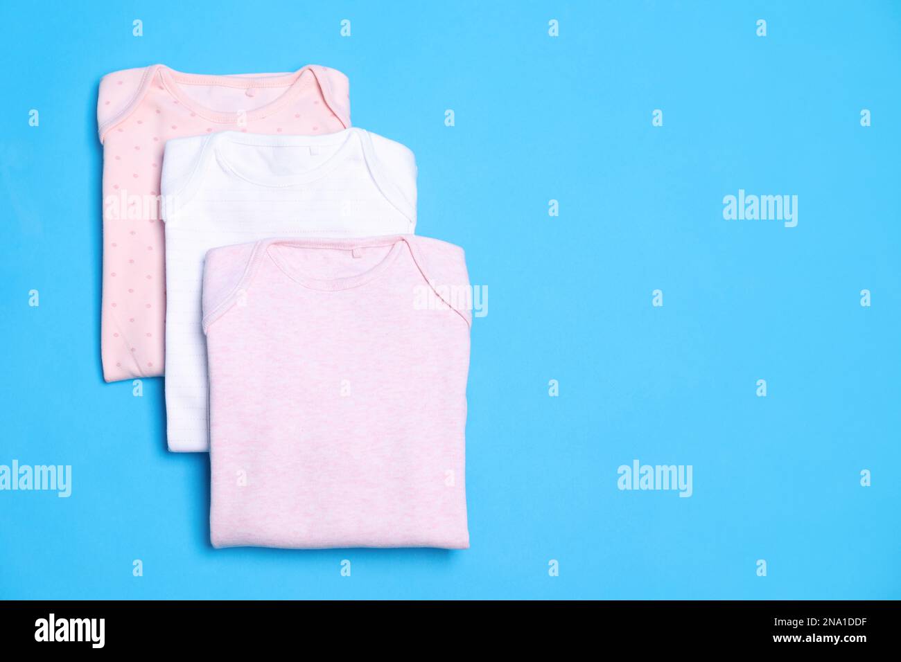 Gefaltete Babyanzüge auf blauem Hintergrund, flach liegend. Platz für Text Stockfoto