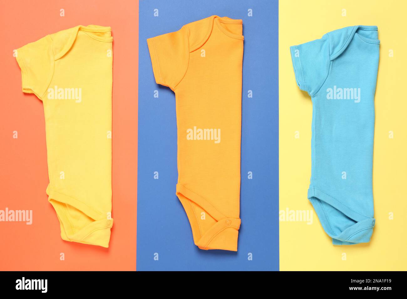 Verschiedene Babyanzüge auf farbigem Hintergrund, flach liegend Stockfoto