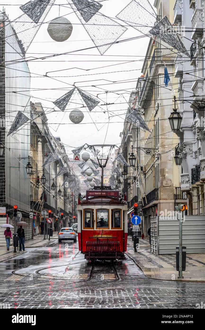 Stadtleben in Lissabon, mit Straßenwagen, Fußgängern und dekorativen Kunstwerken, die über der Straße zwischen den Gebäuden hängen Stockfoto