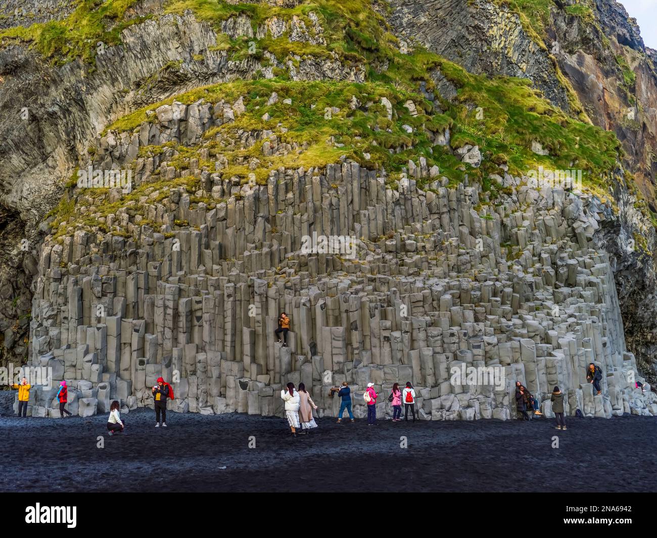 Touristen stehen auf schwarzem Sand und betrachten Basaltsäulen im Süden Islands; Myrdalshreppur, Südregion, Island Stockfoto