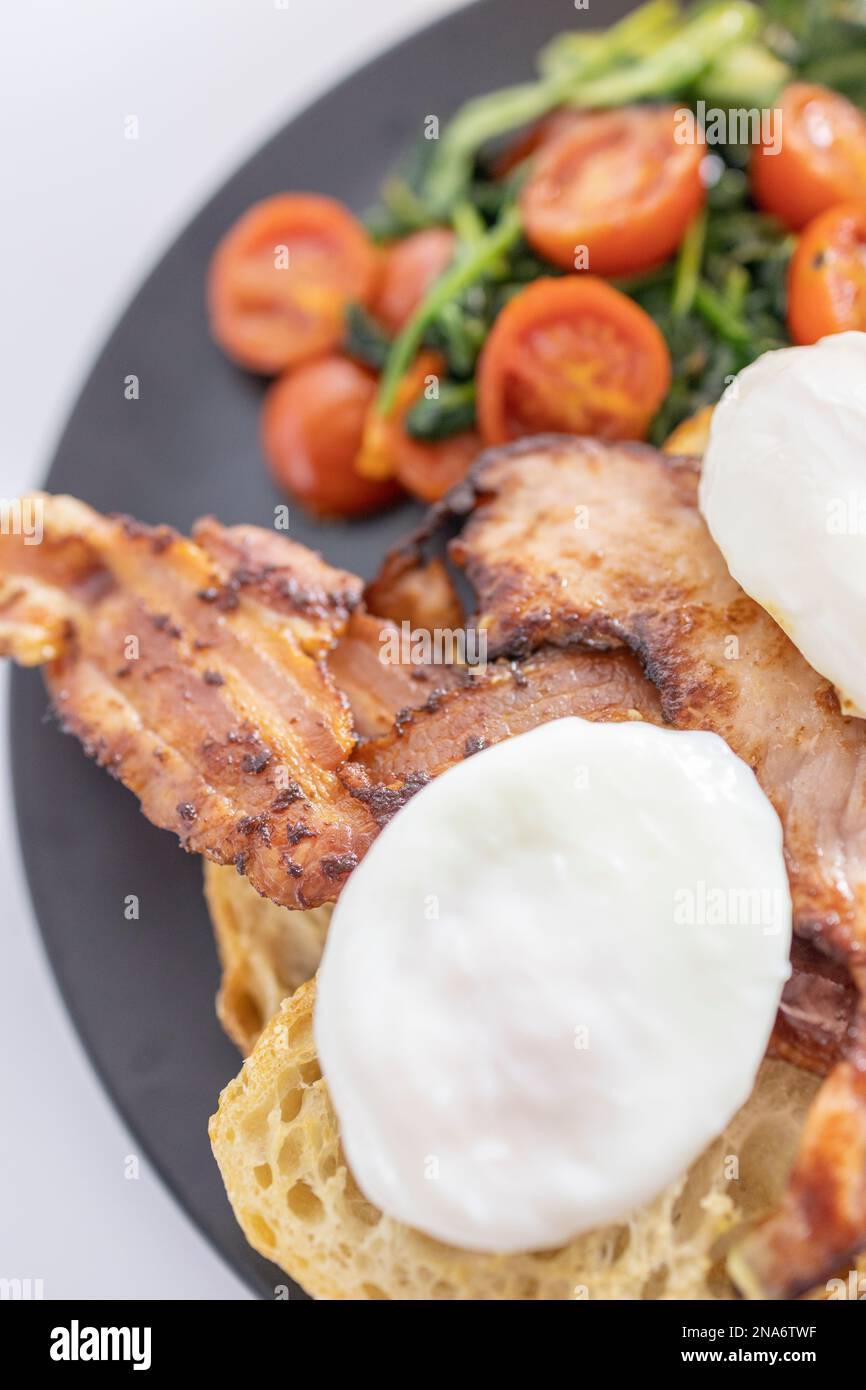 Großes Frühstück, pochierte Eier mit Speck auf Toast mit gebratenen Tomaten und Spinat Stockfoto