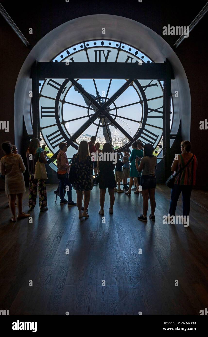 Touristen stehen mit Blick auf die Rückseite einer Uhr aus klarem Glas im Musee D'Orsay mit Blick auf das Riesenrad Grande Roue de Paris; Paris, Frankreich Stockfoto