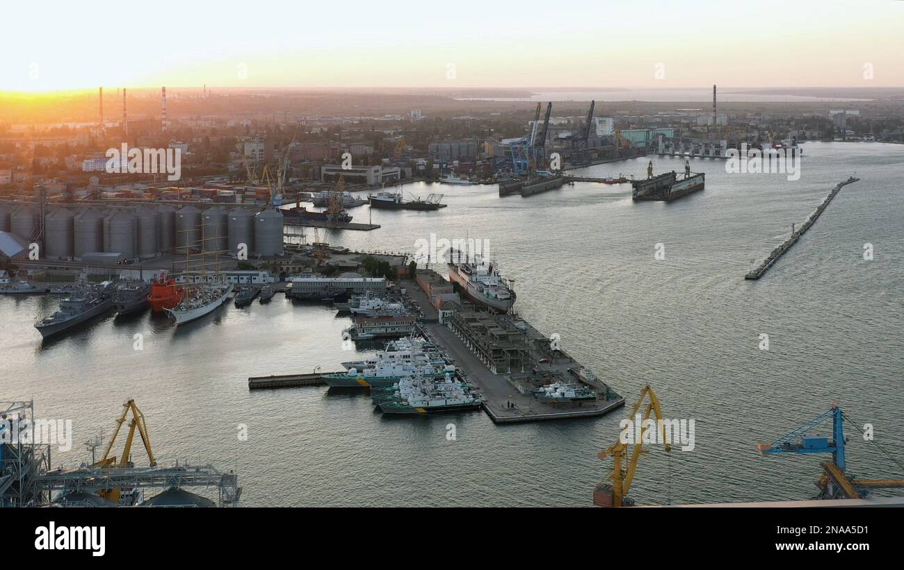 Drohnenansicht des städtischen Seehafens mit Frachtschiffen und Getreideterminals. Abendlicht bei Sonnenuntergang. Stockfoto