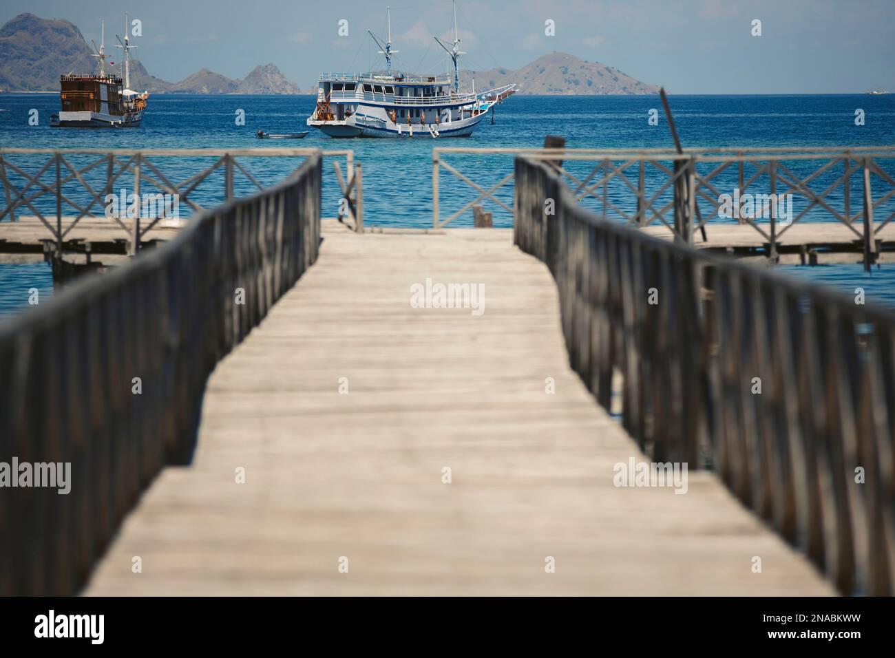 Luxusschiffe, die vor der Küste ankern und von einem Holzpier aus gesehen werden, Komodo Nationalpark; Ost Nusa Tenggara, Indonesien Stockfoto