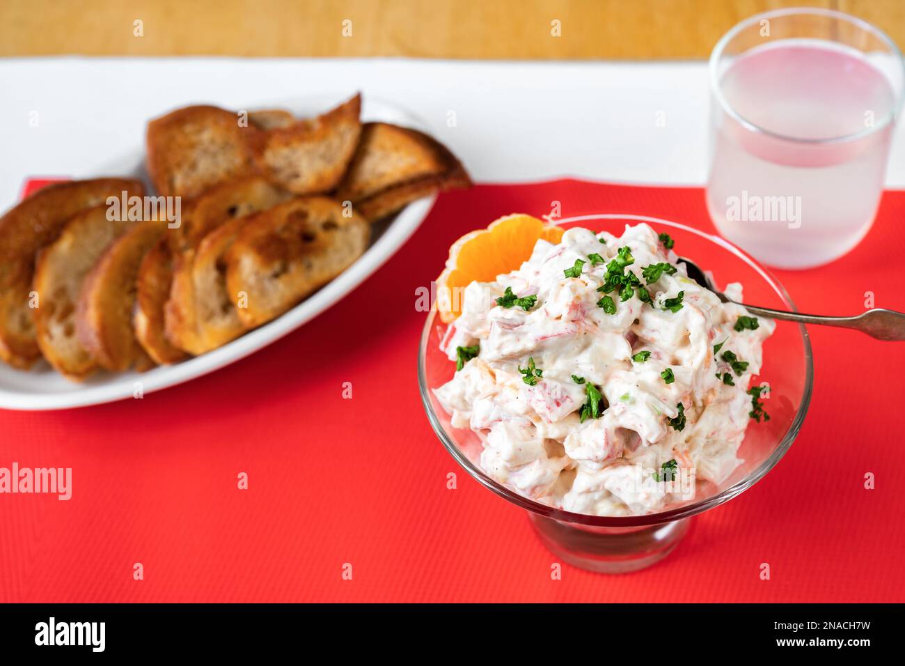 Würziger Krabbensalat in Glasschüssel, gebratener Toast und Limonade auf rotem Tischtuch auf dem Tisch. Stockfoto