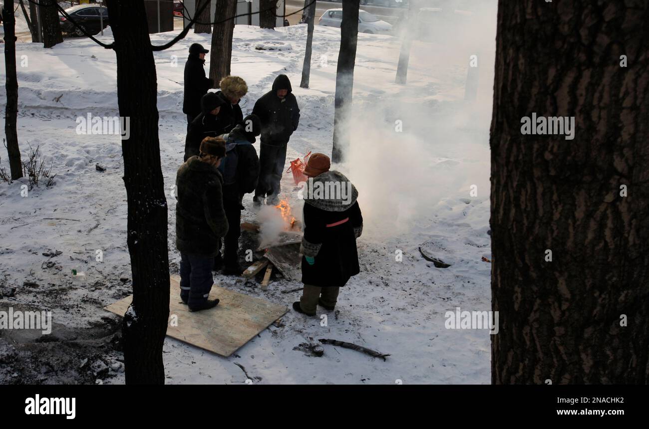 Homeless people stand around a fire warming up as they wait for a free dinner provided by Russian Orthodox church near a railway terminal in Moscow, Wednesday, Feb. 1, 2012. In Moscow temperatures fell to minus 21 C (minus 6 F). (AP Photo/Alexander Zemlianichenko) Stockfoto