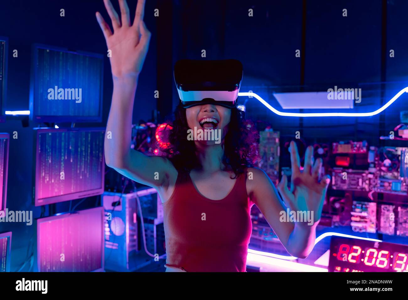 Junge Asiatin, die eine Virtual-Reality-Brille im Dunkeln benutzt, mit Neonbeleuchtung voller Computer und Technologie Stockfoto