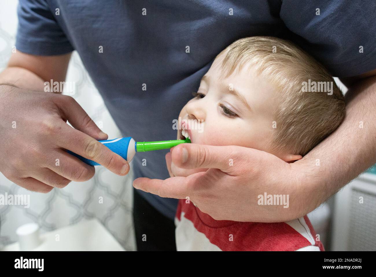 Dad hilft dem Kind, Zähne mit einer farbenfrohen elektrischen Zahnbürste zu putzen Stockfoto