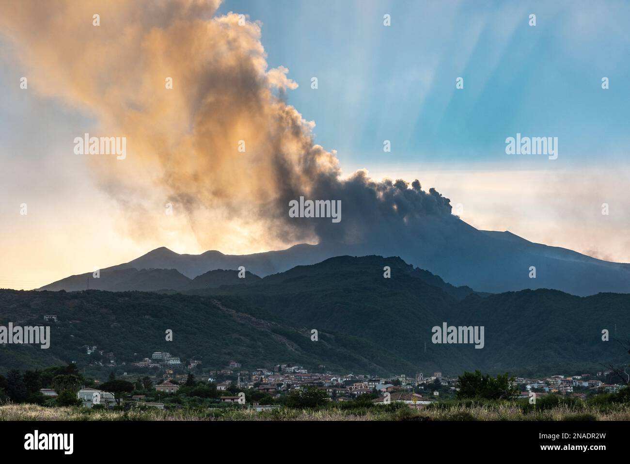Dichte Wolken vulkanischer Asche, die aus den Kratern auf dem Ätna, Sizilien, emittiert werden, der über der Stadt Zafferana Etnea im Vordergrund thront Stockfoto