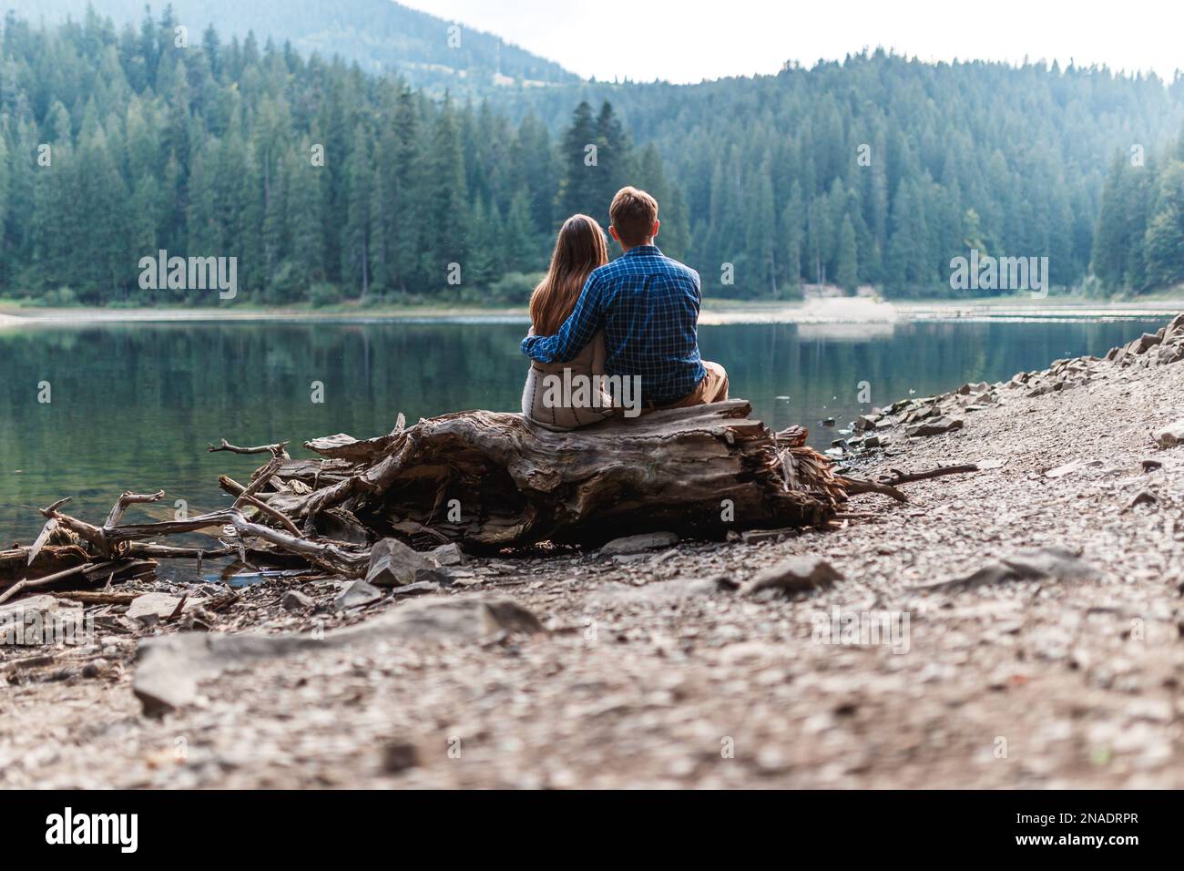 Ein Mann und eine Frau sitzen am See in den Bergen und umarmen sich Stockfoto