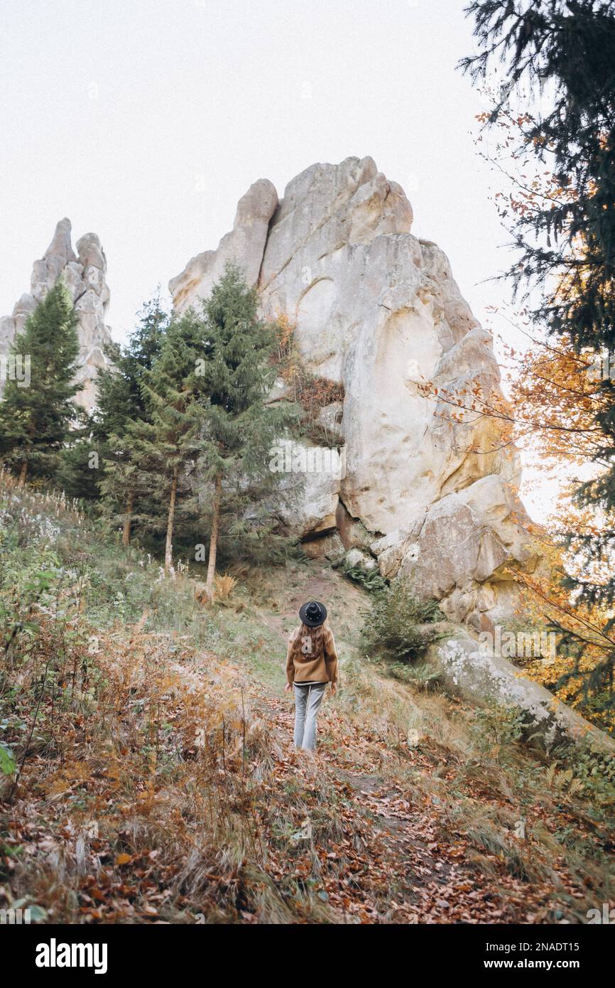 Eine Frau mit Jacke und Hut läuft durch den Wald in der Nähe der Berge Stockfoto