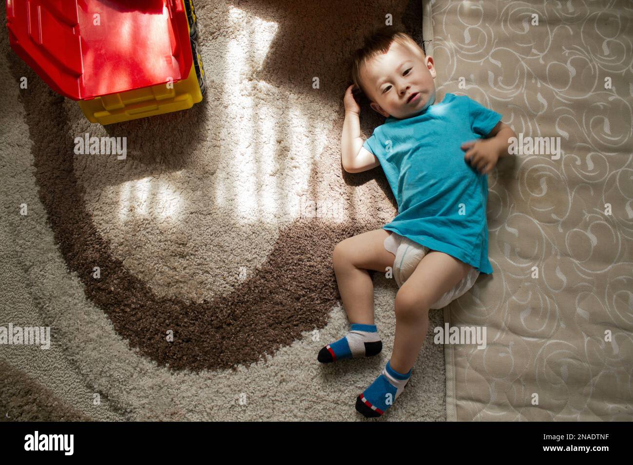 Der kleine Junge liegt auf dem Teppich neben der Matratze Stockfoto