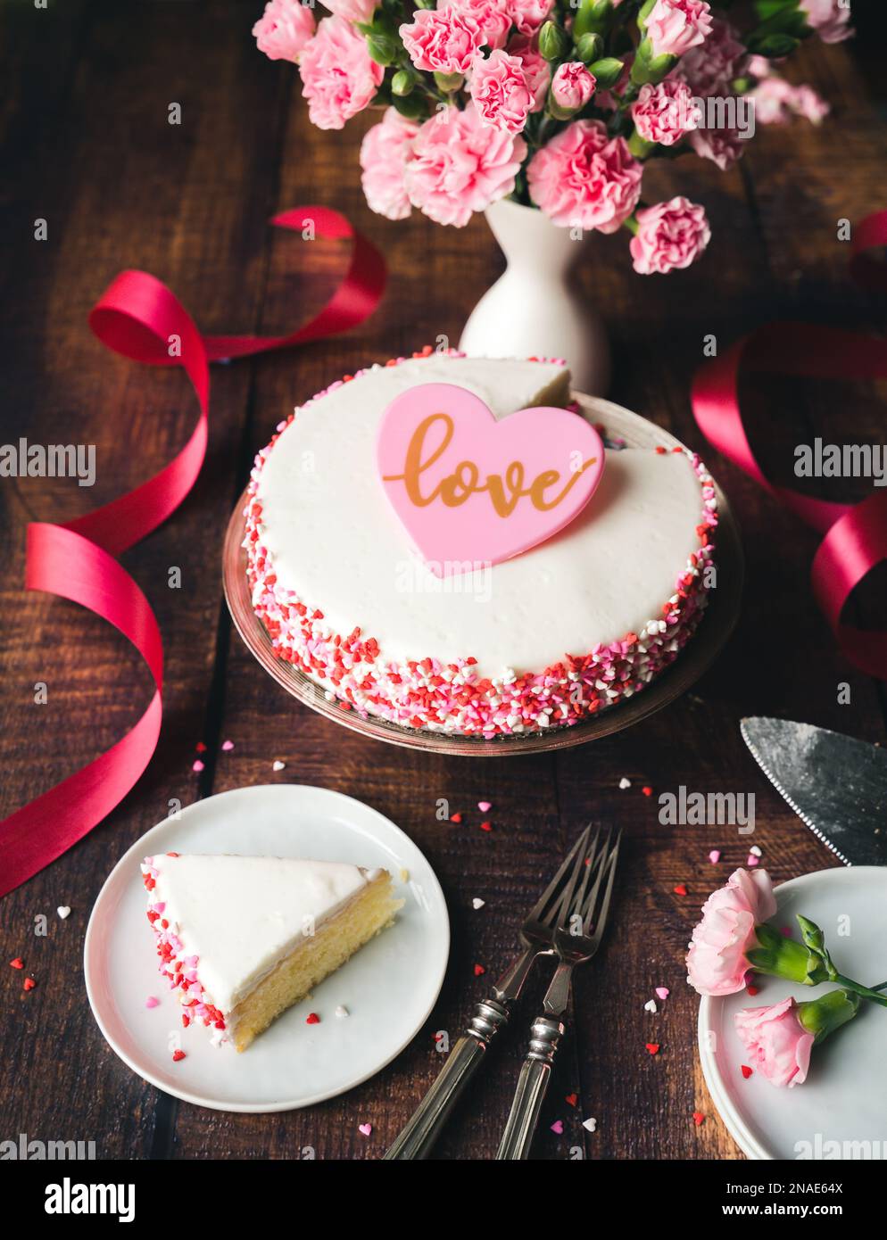 Valentinstag-Kuchen mit Herzstreuseln und Blumen auf einem Holztisch. Stockfoto