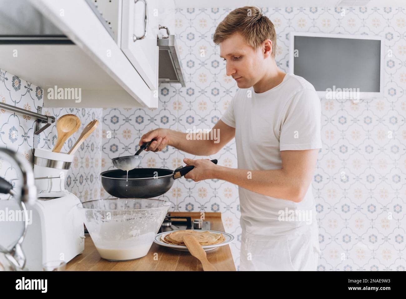 Ein junger Mann in Weiß, der Spaß hat, kocht Pfannkuchen Stockfoto
